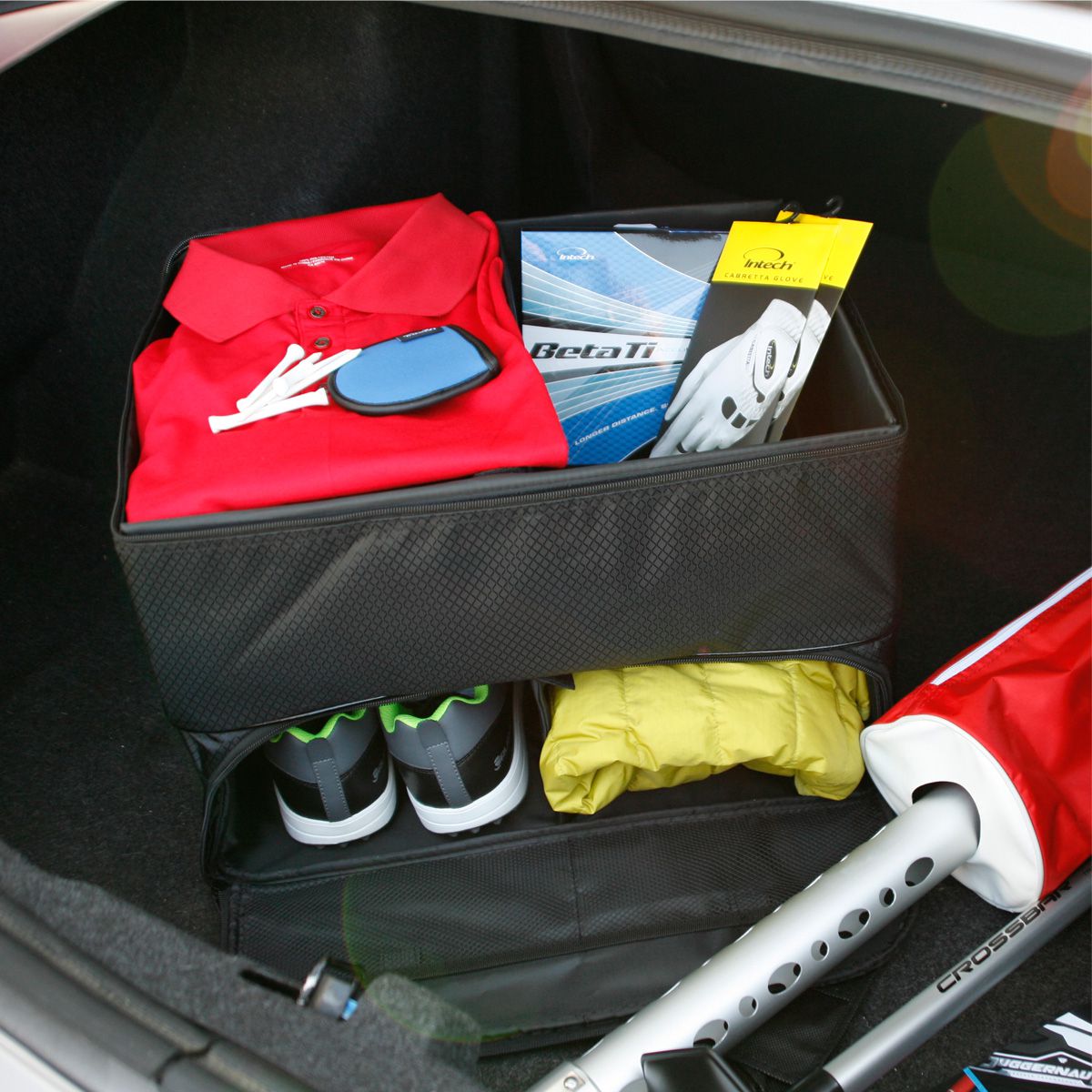 an Intech Double Row Golf Trunk Organizer inside a car trunk with golf apparel inside
