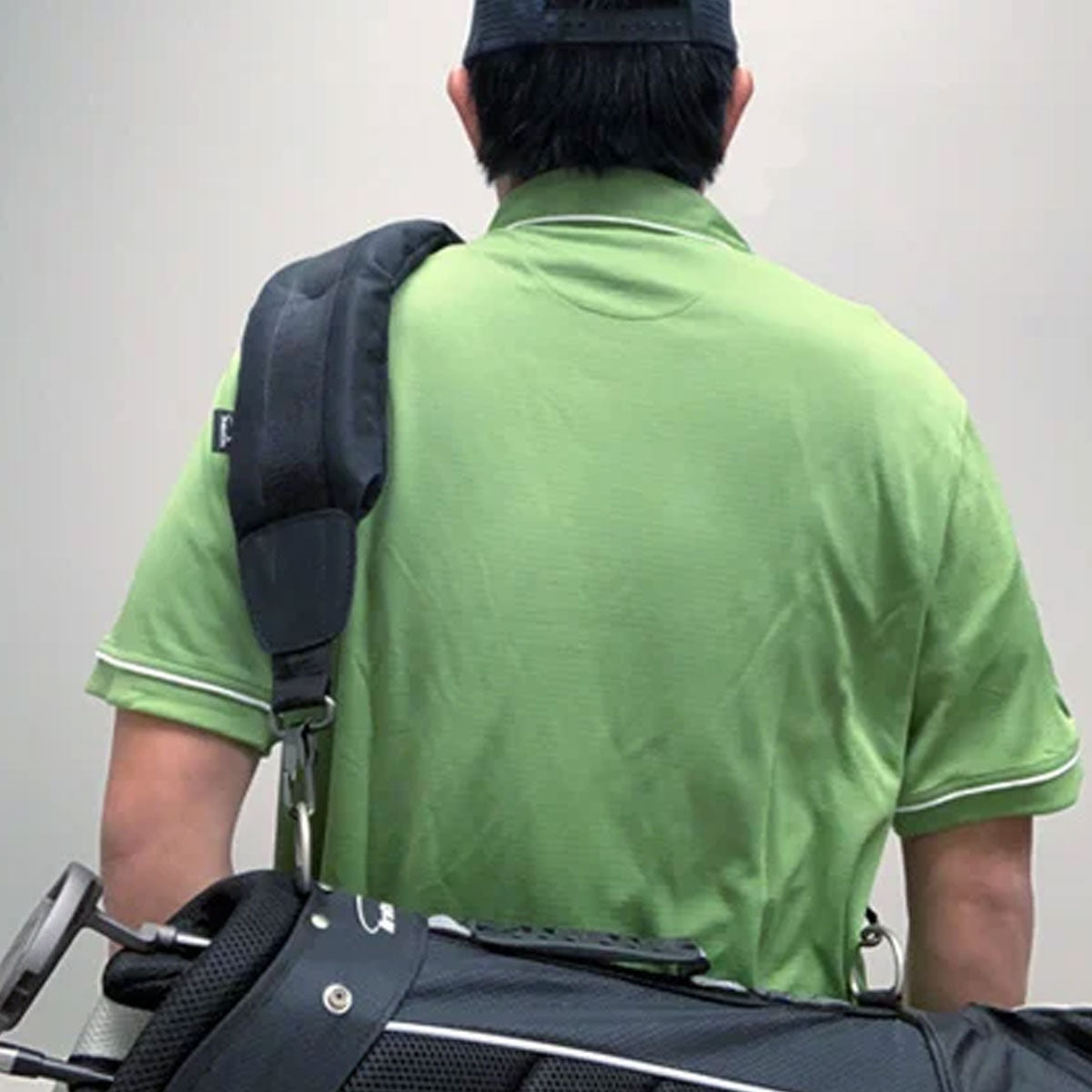 person carrying on their left shoulder an Intech Single Padded Adjustable Golf Bag Strap attached to a black golf bag